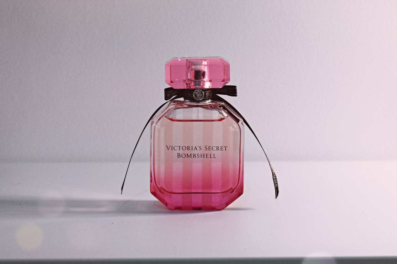 Stylish pink perfume bottle with bow and intricate cap on a white surface.